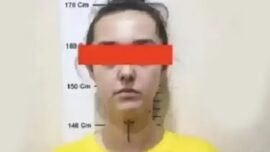 Foto seseorang di depan papan pengukur tinggi badan bergaya foto kepolisian. Mata ditutupi balok merah dan mengenakan kaus kuning
