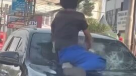Seorang pria berdiri di atas kap Toyota Fortuner hitam sambil memukul kaca depan kendaraan yang telah retak, saat mobil tersebut dikerumuni warga di kawasan Tanah Abang, Jakarta Pusat.