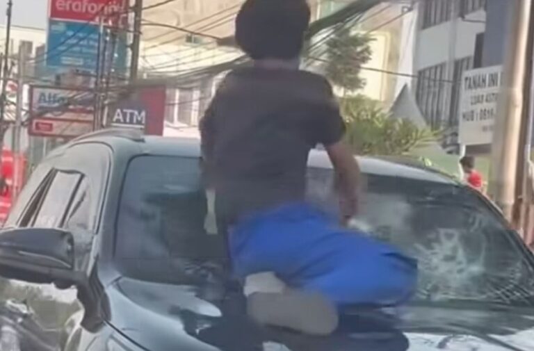 Seorang pria berdiri di atas kap Toyota Fortuner hitam sambil memukul kaca depan kendaraan yang telah retak, saat mobil tersebut dikerumuni warga di kawasan Tanah Abang, Jakarta Pusat.