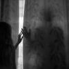 Ilustrasi perempuan ketakutan mengintip dari balik tirai jendela pada malam hari setelah dugaan pengintaian di sekitar rumah.