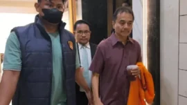 Roy Suryo menenteng rompi tahanan berwarna oranye dan minuman saat berpindah dari satu ruangan ke ruangan lainnya di Polda Metro Jaya.